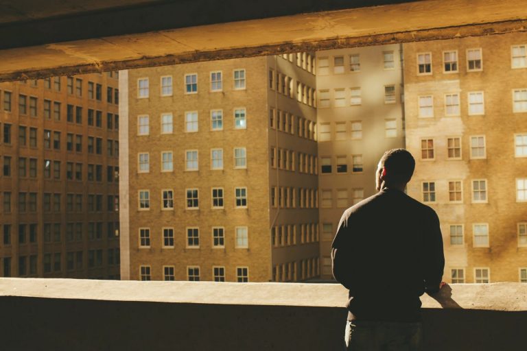 person standing looking out a window at buildings.
